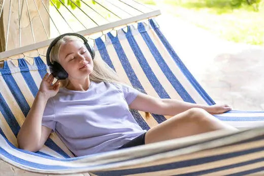 jeune femme écoutant de la musique avec ses écouteurs dans son hamac rayé bleu et blanc