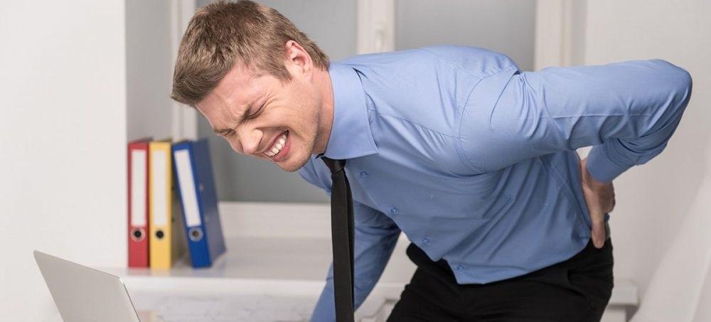 homme pris de douleurs au dos devant un macbook
