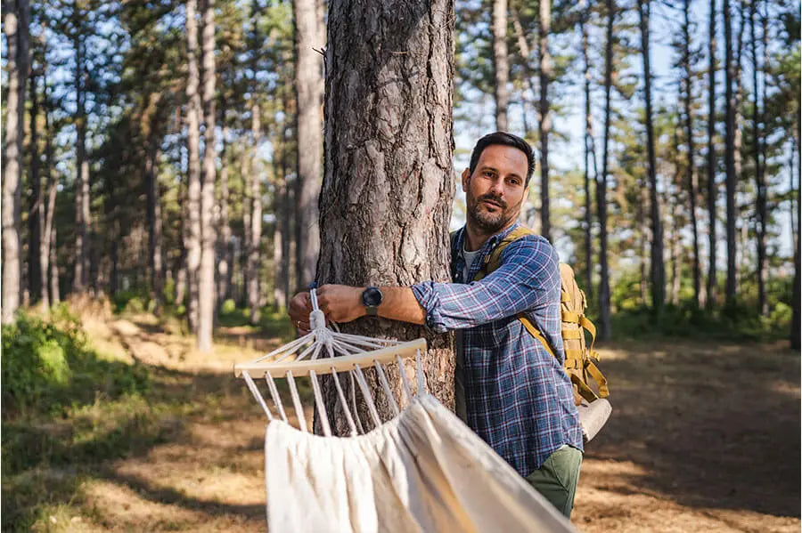 Un randonneur attache un hamac à un arbre solide dans une zone boisée, se préparant à une expérience relaxante en plein air.
