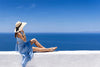 femme avec un chapeau sur un muret blanc en grèce devant un ciel et une mer bleu