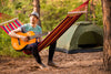 homme dans un hamac coloré jouant de la guitare en camping